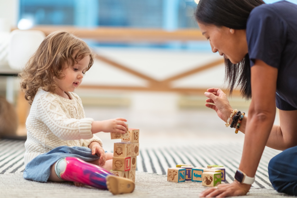 Young girl sitting on the floor with building blocks with her occupational therapist