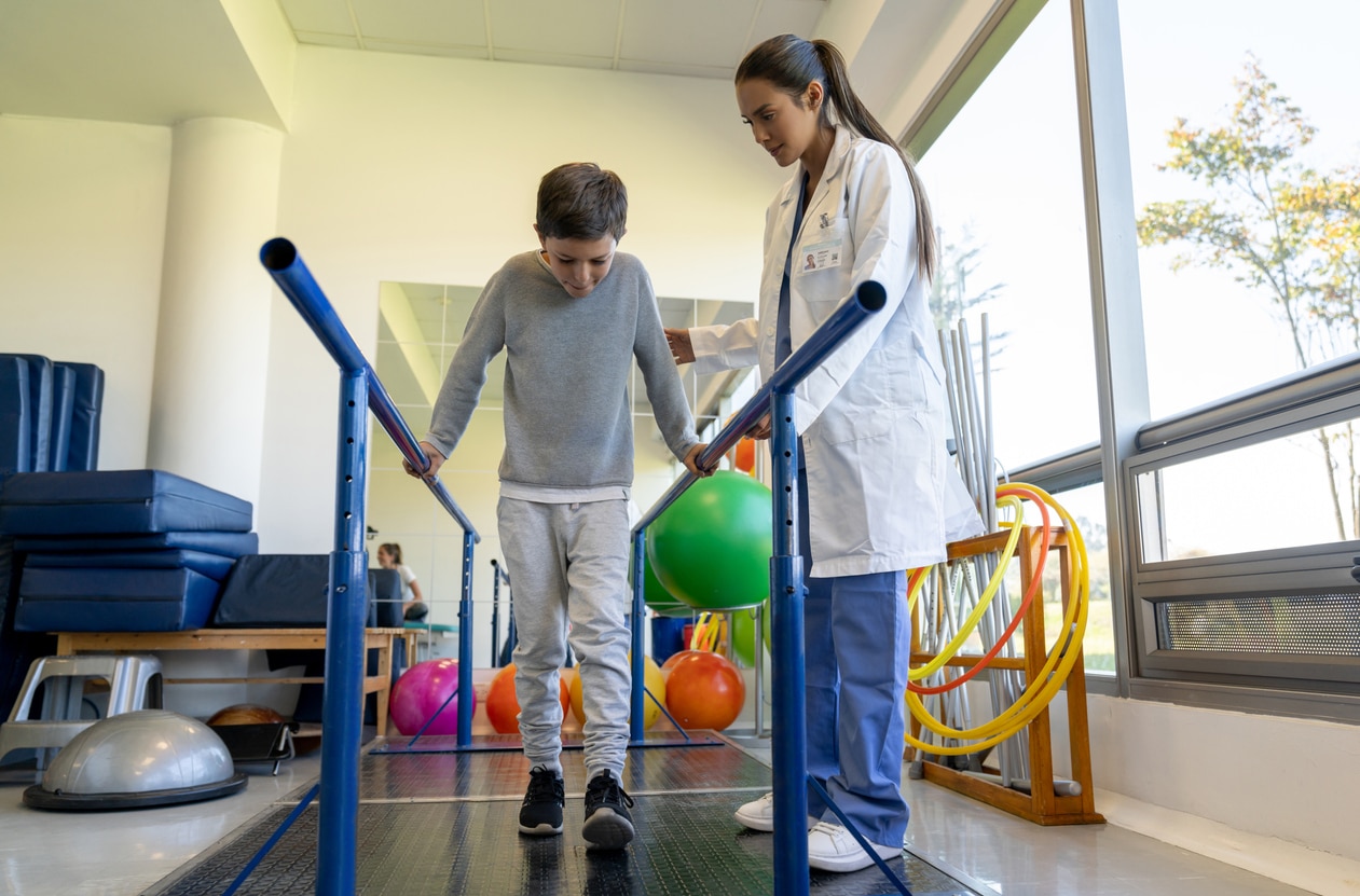 Boy using hand rails to walk while being spotted by his physical therapist