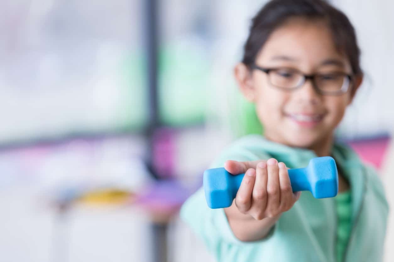 Young girl holding a dumbbell up in front of her during physical therapy