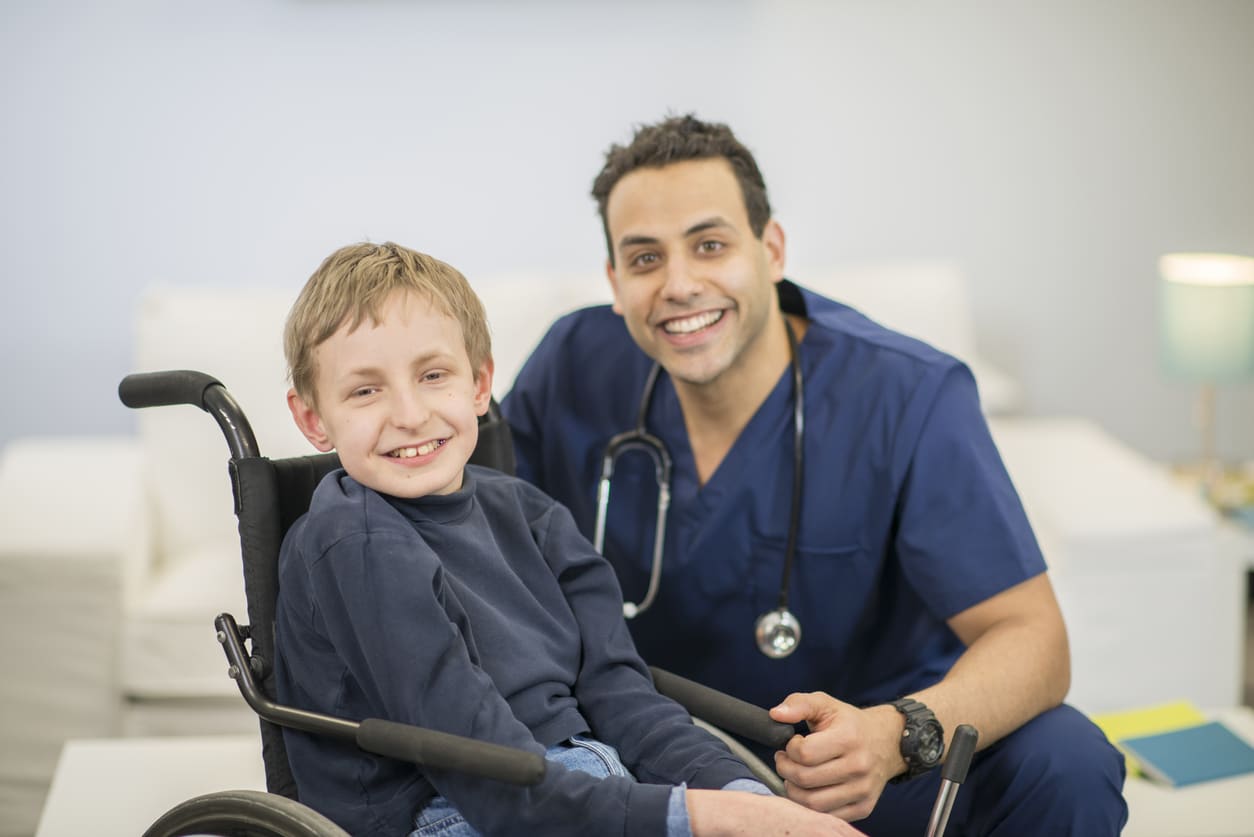 Young boy in a wheelchair smiling next to his physical therapist