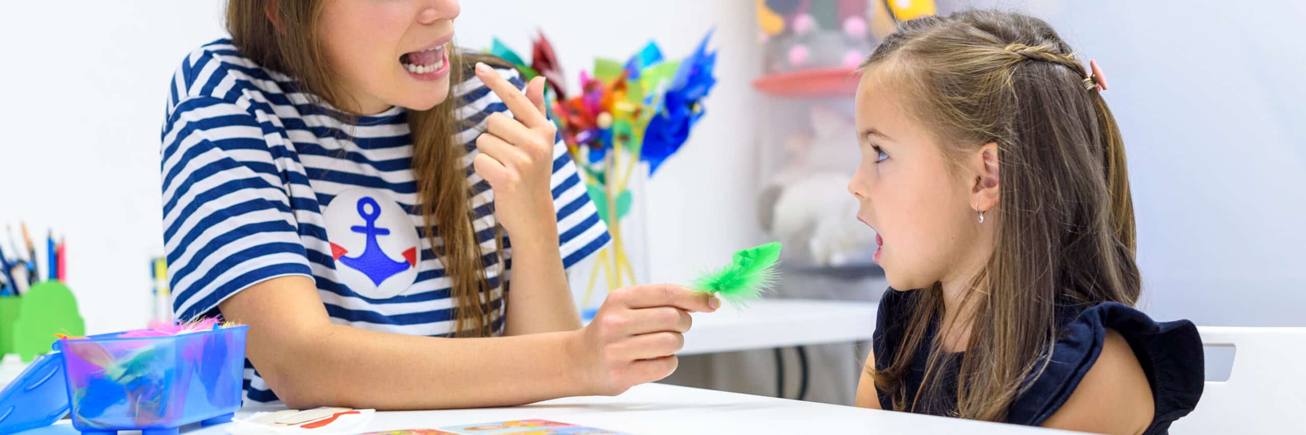 Female speech therapist holding up a letter and practicing verbal sounds with a child in pediatric speech therapy