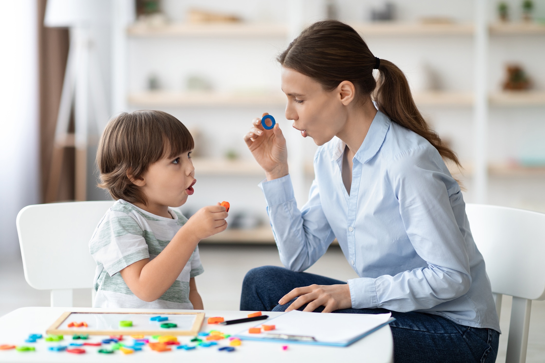 Speech therapist practicing sounds of letters at a table with a young child during pediatric speech therapy