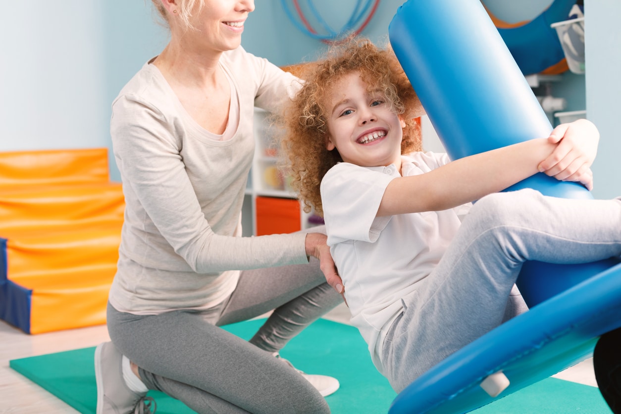 Boy swinging while being pushed in pediatric occupational therapy by his therapist